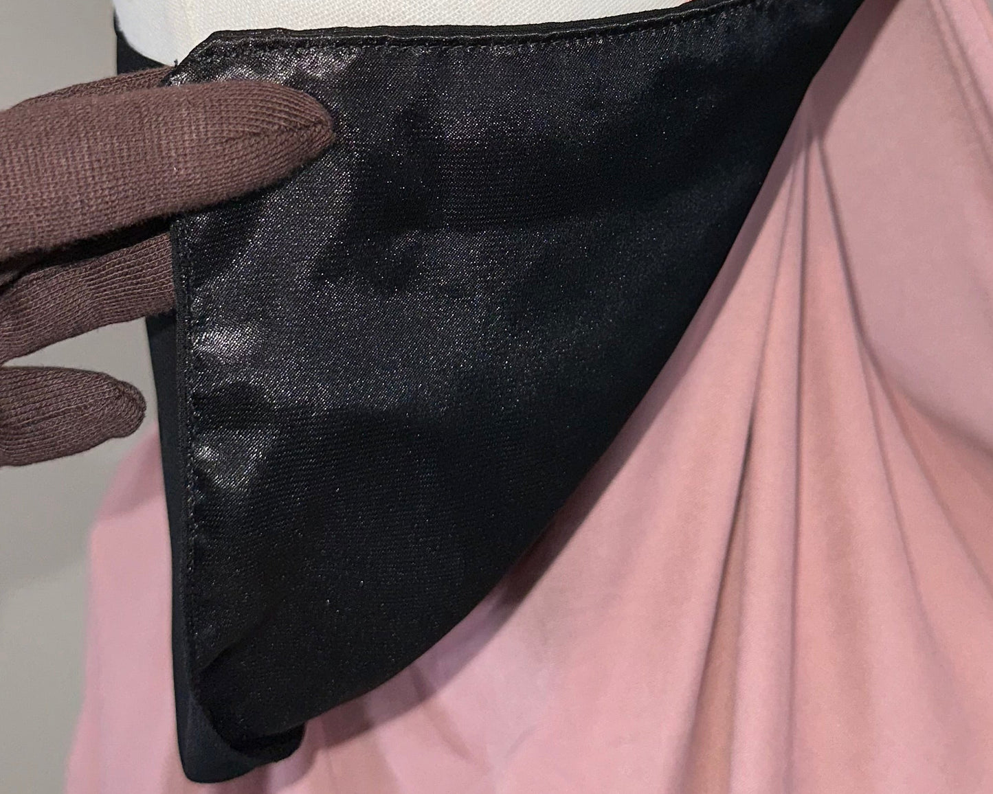 Hand wearing brown glove holding black satin fabric with pink and white cloth background