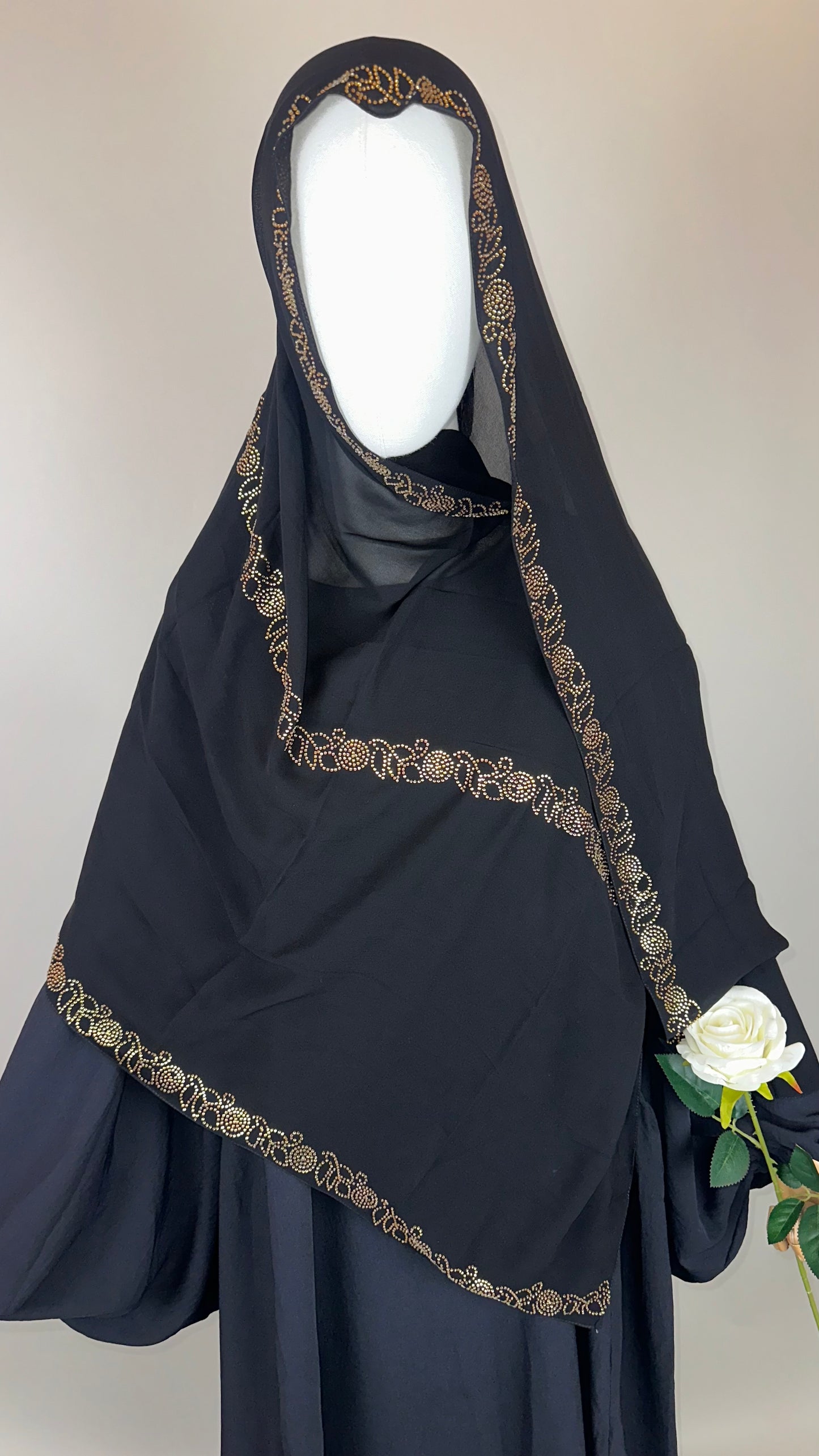 Black khimar with gold embroidery, mannequin holding white rose, modest Islamic fashion