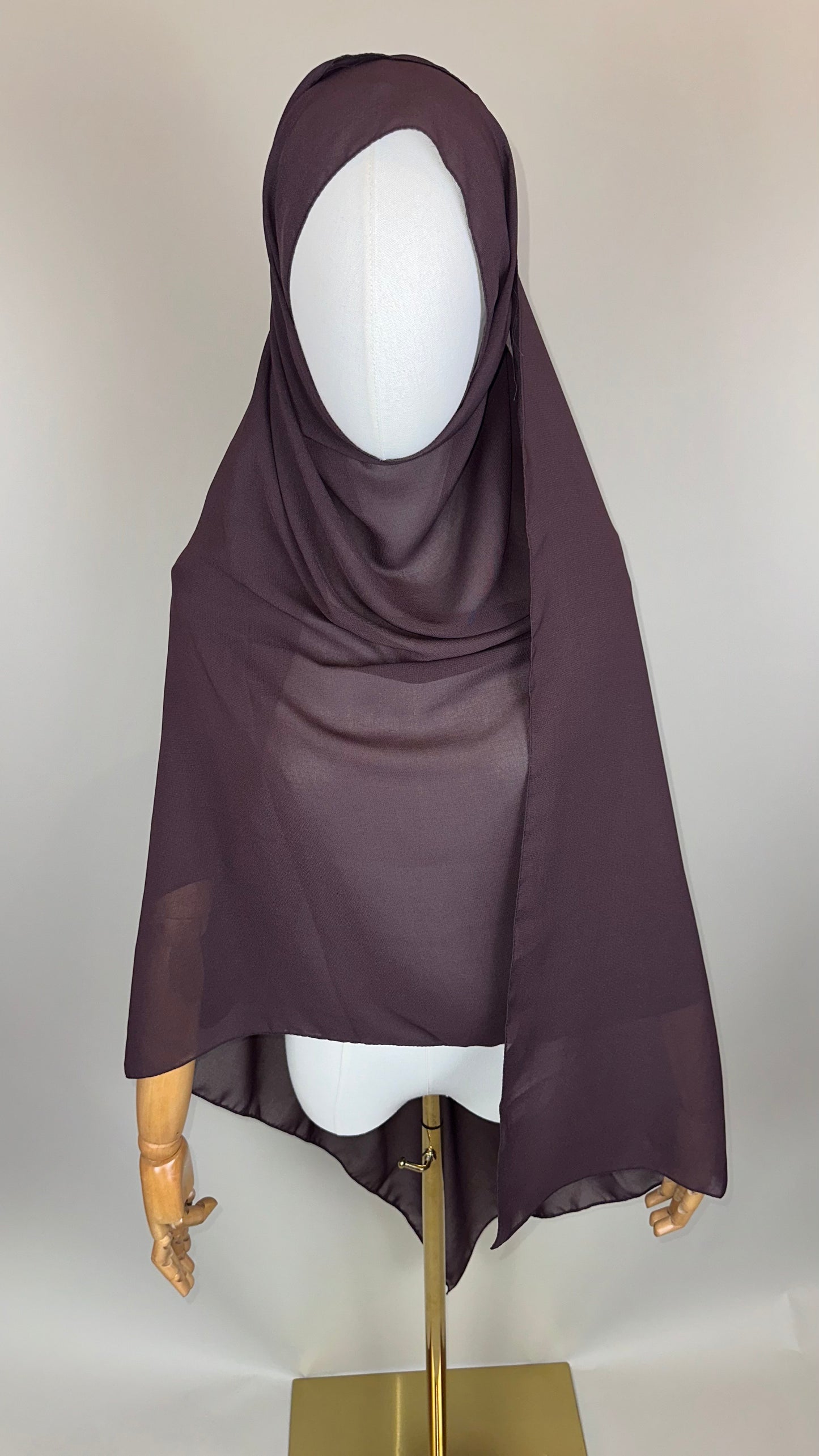 Brown chiffon hijab on mannequin with wooden arms, gold stand, neutral background