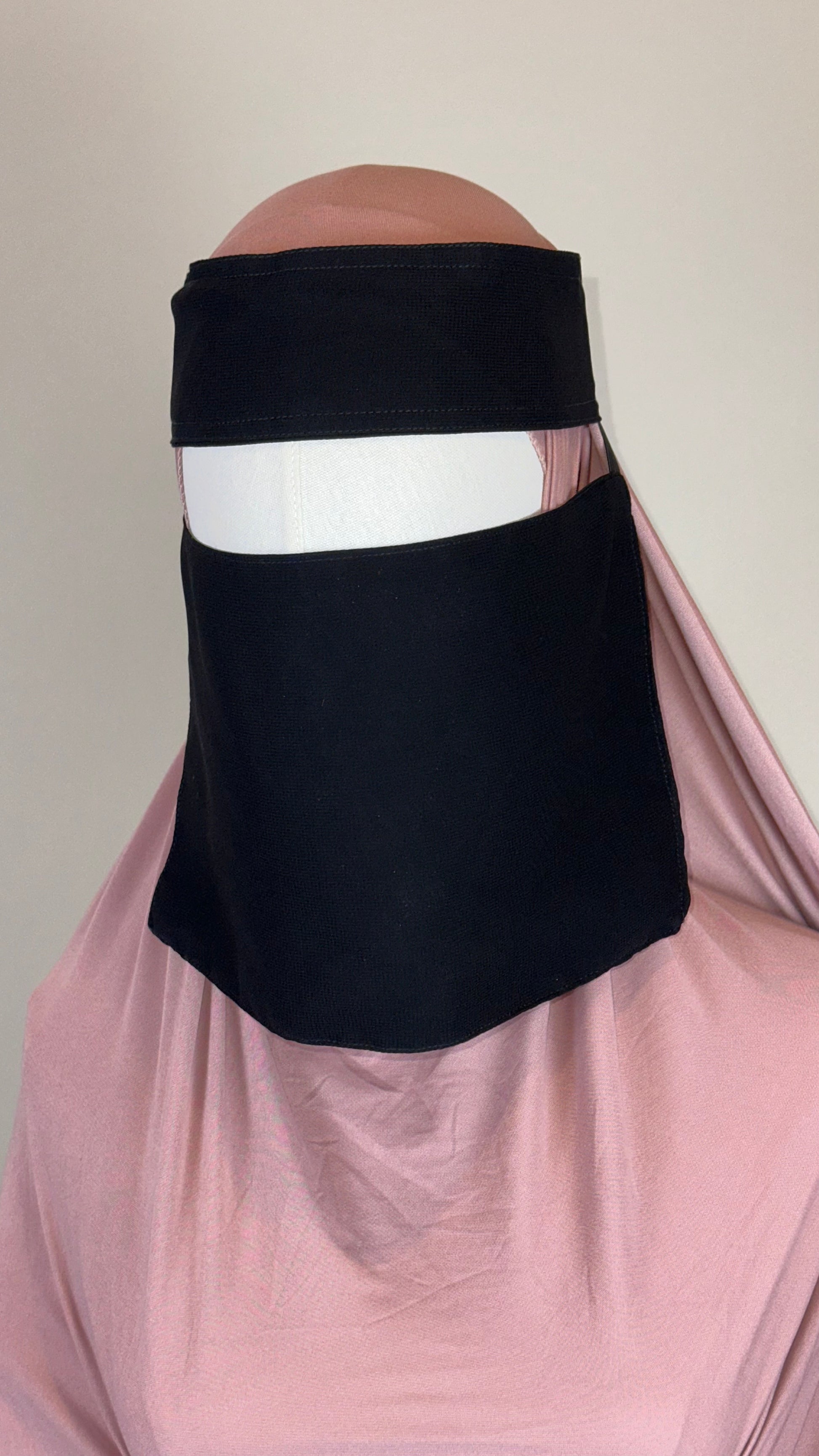 Black niqab face covering on mannequin with light pink hijab