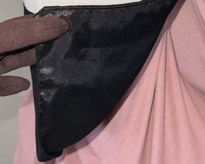 Hand wearing brown glove holding black satin fabric with pink and white cloth background