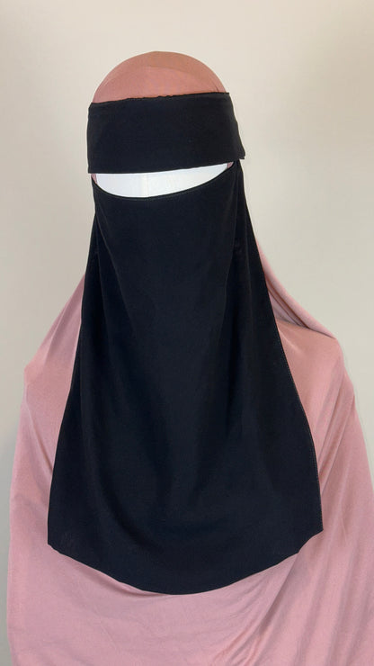 Mannequin wearing a black niqab and pink hijab against a plain background