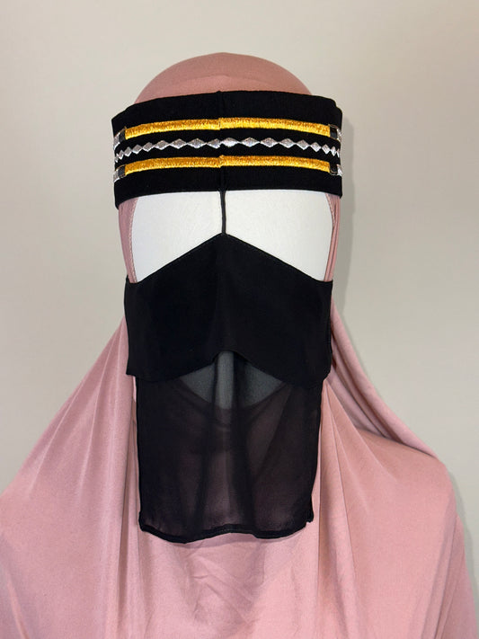 Black Saudi niqab with gold trim and embroidery, worn over pink hijab