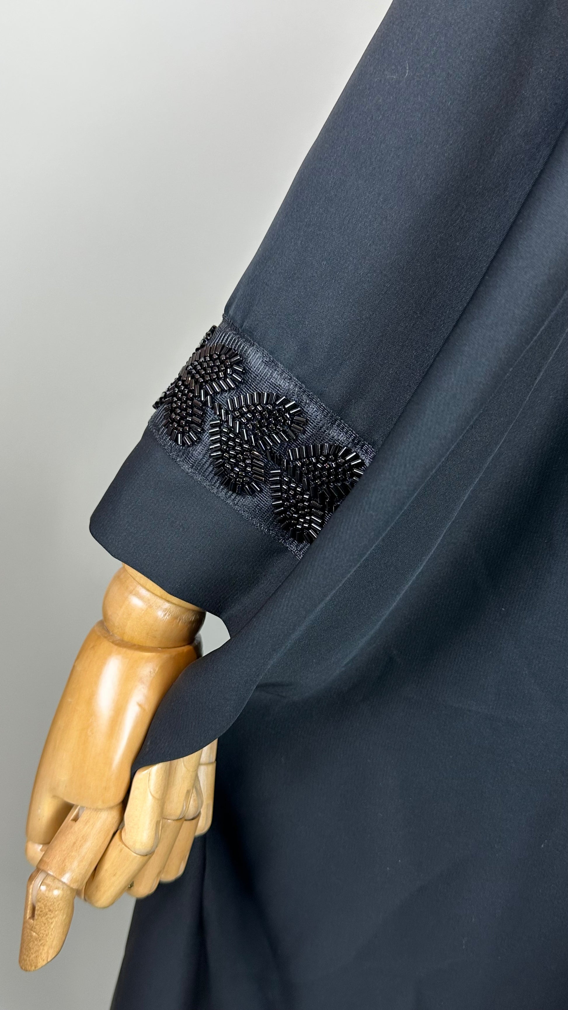 Black sleeve with beaded leaf embroidery detail, shown on a wooden mannequin hand