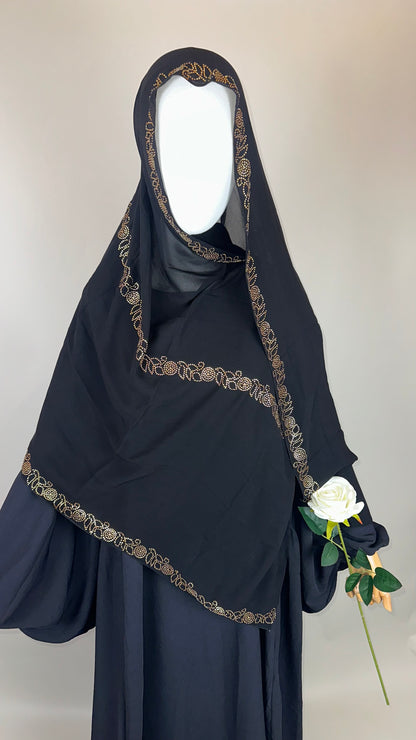 Black embroidered hijab with gold trim, mannequin holding white rose, neutral background
