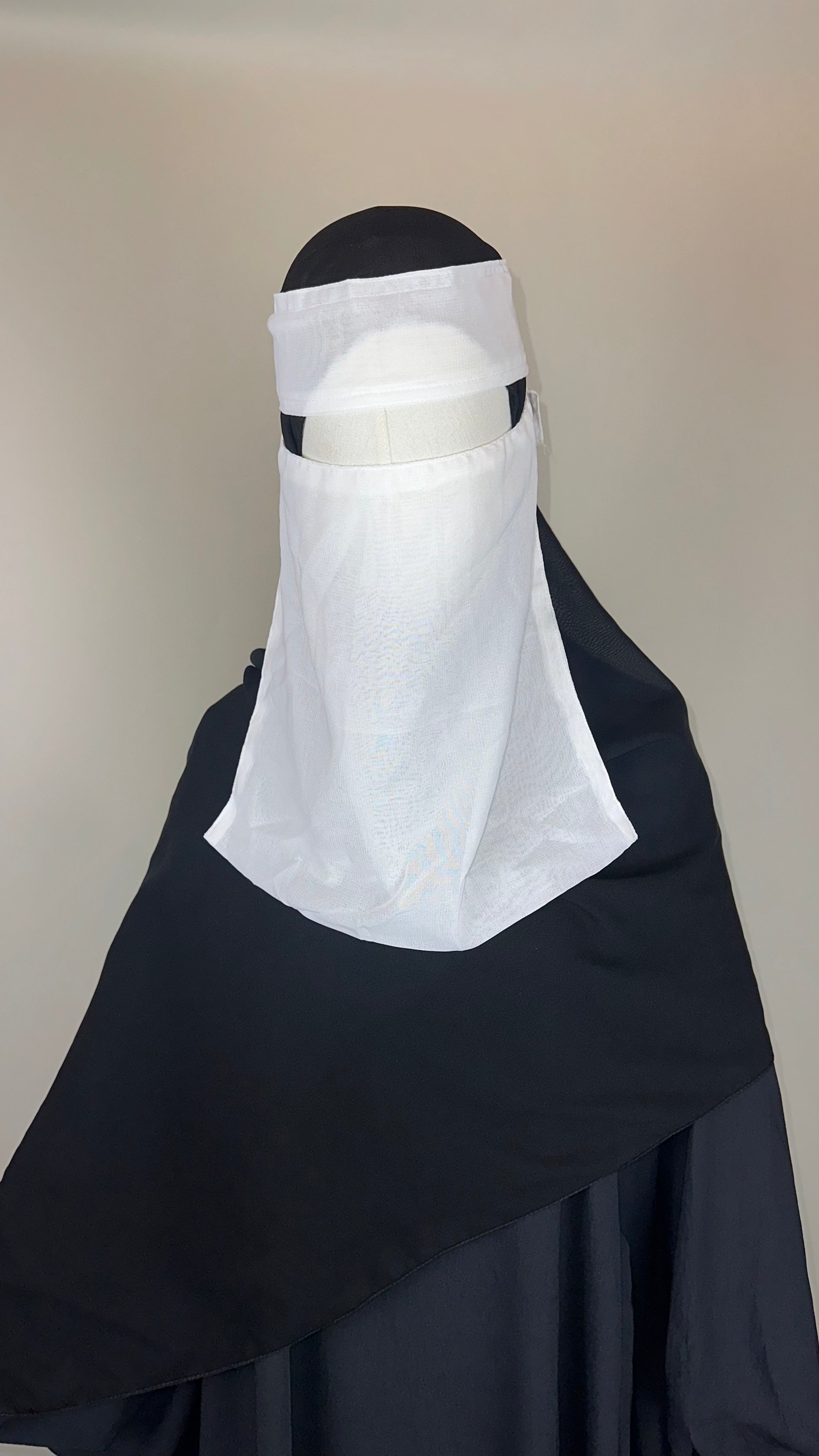 Black abaya and white niqab on mannequin against plain background