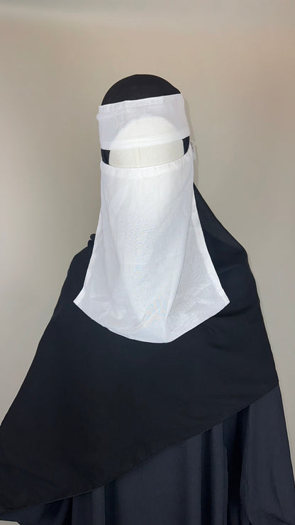 Black abaya and white niqab on mannequin against plain background