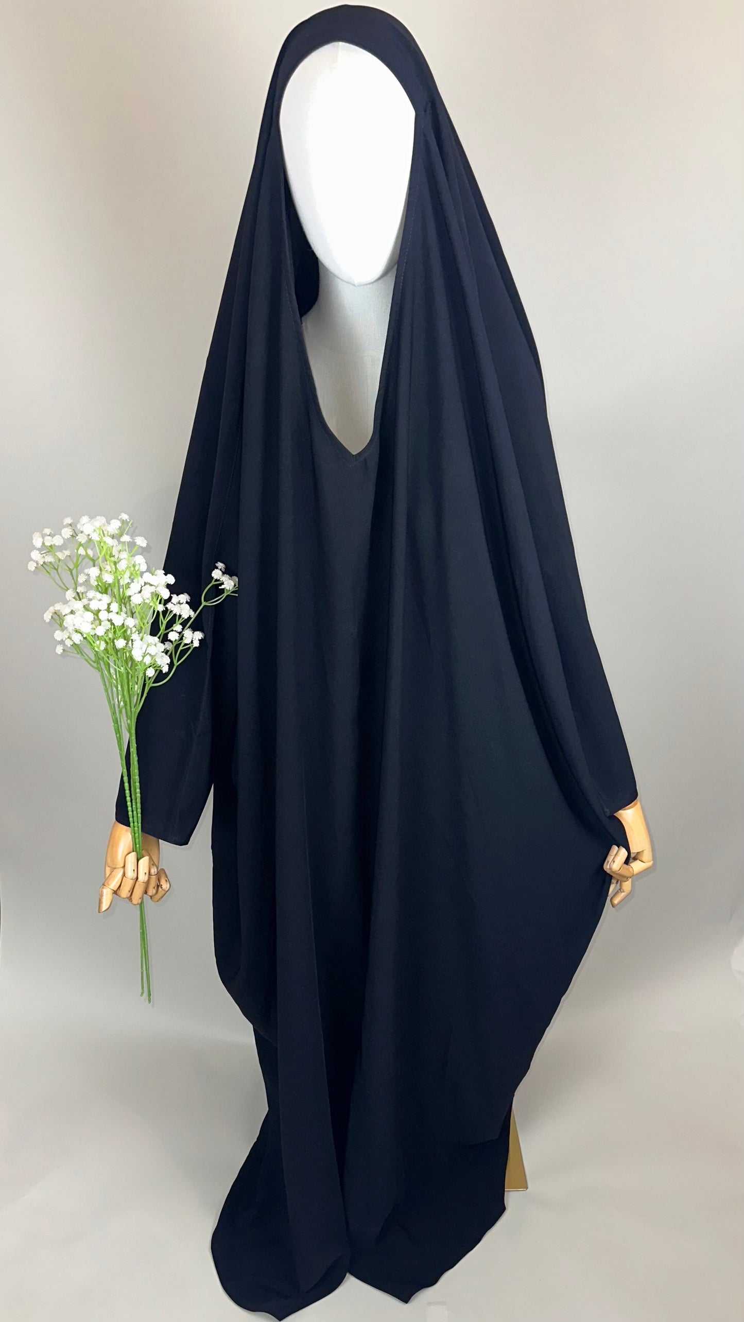 Mannequin in black abaya holding white flowers, plain background